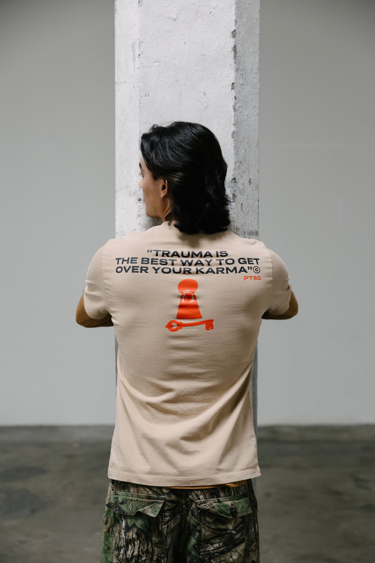 A model wearing a 11:11 L.U.C.K. PTSD UNISEX T‑SHIRT, with "Trauma is the best way to get over your karma" written on the back